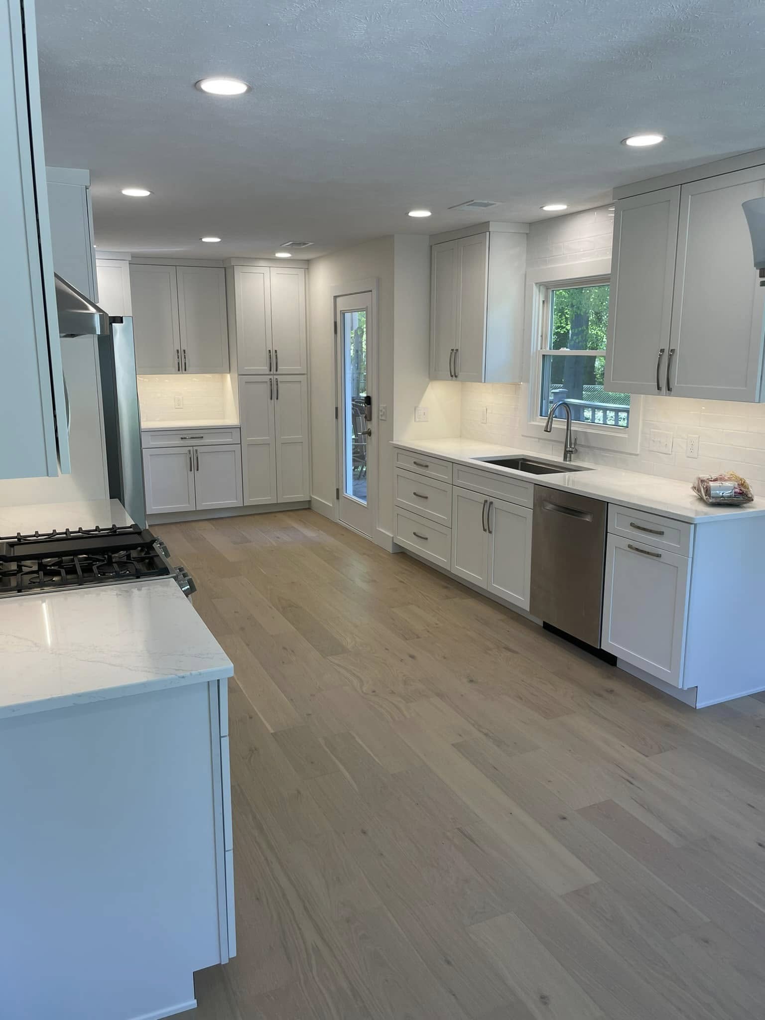 Modern kitchen remodel featuring light gray cabinets, white countertops, stainless steel appliances, and wood-look flooring.