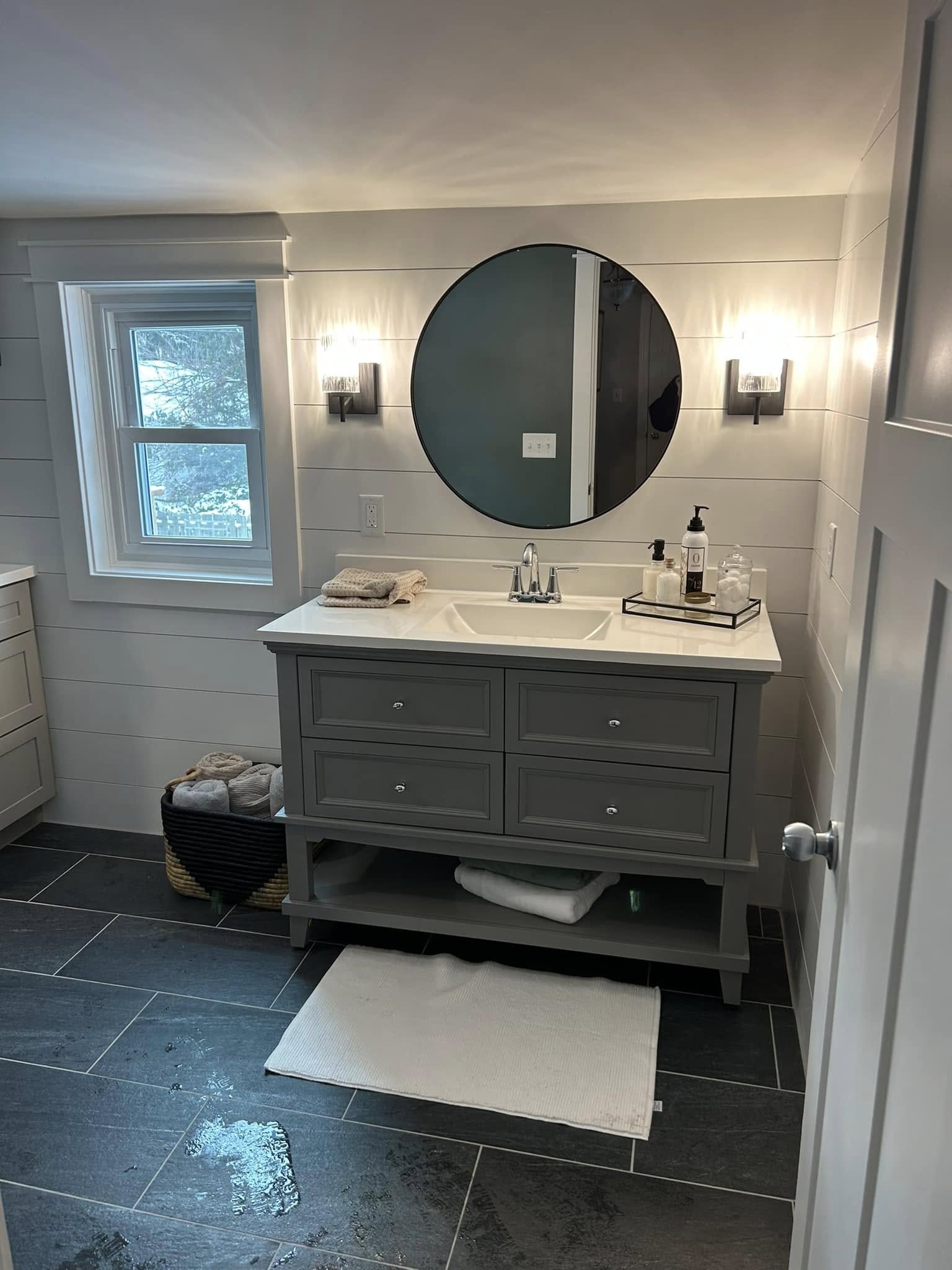 Remodeled bathroom with modern vanity, circular mirror, updated lighting, and fresh paint