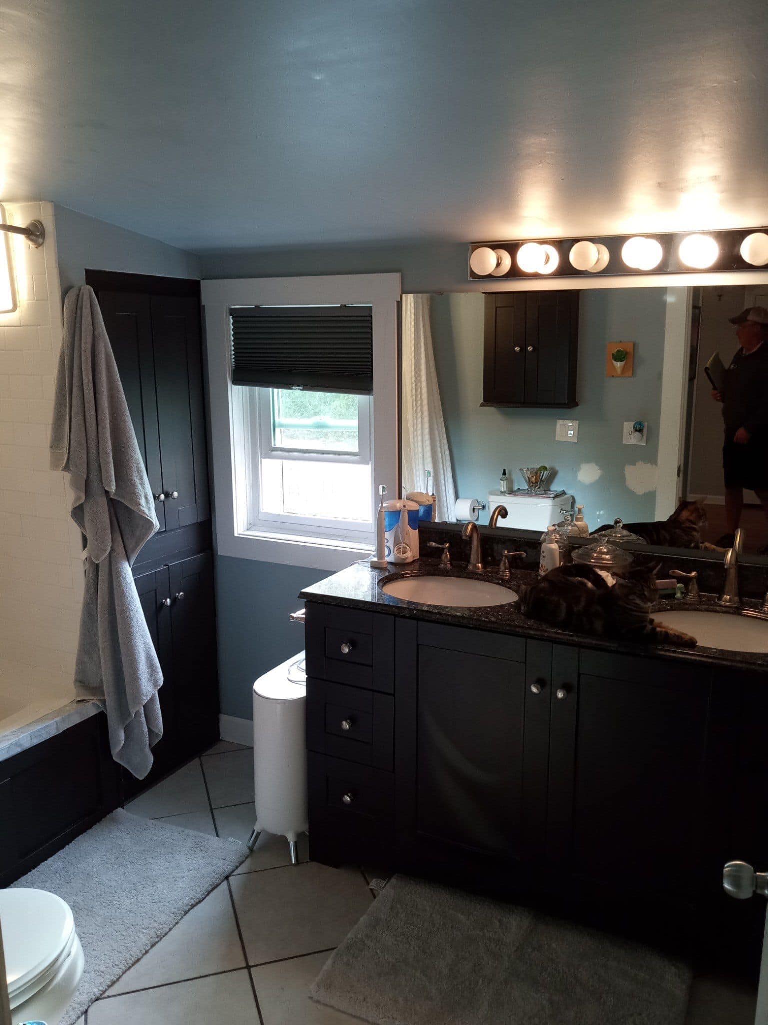 Small outdated bathroom with dark vanity, tile flooring, and minimal lighting
